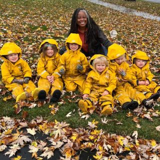 teacher and children in a pile of fall leaves
